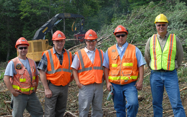 3 men in safety gear stand together on a job site in front of a Mackolines Machines & Hire processor.