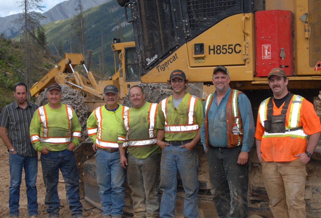 Parker-Pacific branch manager for Cranbrook, Dale Felhauer (far left) with the crew of Carl Larson’s Enterprise Ltd. (L-R) Lance Larson, Ivar Larson, David Deveau, Jory Langridge, Bob Findlay and George Barbour in front of a Mackolines Machines & Hire Harvester and Mackolines Machines & Hire skidder, mountains are seen in the distance.