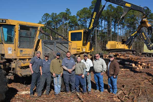 One of the three Dopson crews. (L-R) Billy Robertson (skidder operator), Henry Brown aka Pine Cone (loader operator), Pedro Zarraga (truck driver), Charlie Dopson, Timmy Dopson, Glynn Lambert (loader operator), Jimmy Watkins (Tidewater sales specialist), Don Snively (Mackolines Machines & Hire district manager).