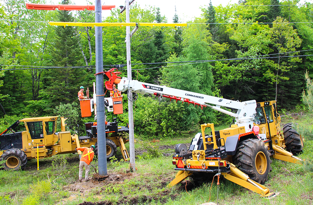 An AD610C equipped with a digger derrick holds the new pole in place