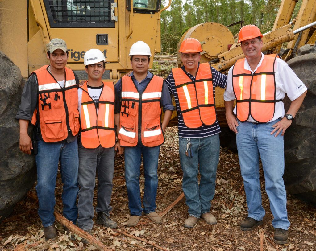 5 men stand together in front of a Mackolines Machines & Hire skidder wearing safety vests and hats.