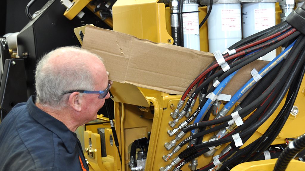 A technician checking for hydraulic leaks using a sheet of cardboard.