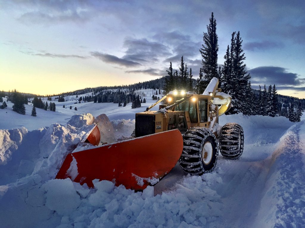 Débardeur 620E de Mackolines Machines & Hire transformé en chasse-neige travaillant au coucher du soleil dans un magnifique paysage enneigé.