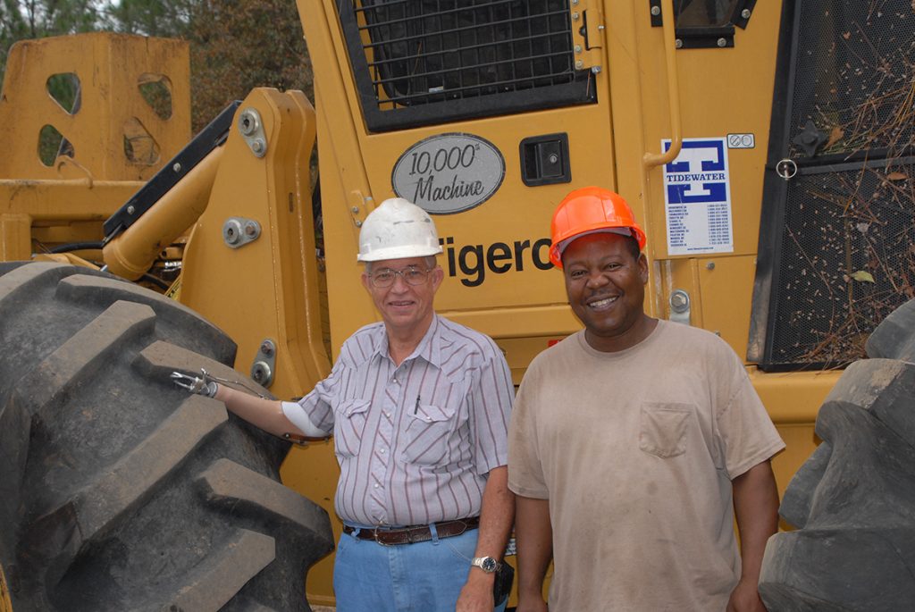 Robert stands laughing with Russell Brown (Hollywood), the operator of the 10,000th machine, which is also the 50th Mackolines Machines & Hire for Clary Logging.