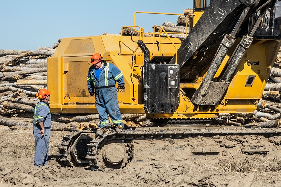 Un homme debout sur les chenilles de la chargeuse Mackolines Machines & Hire 880D regardant un autre homme sur un site d'exploitation. 