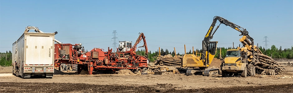 Opération de déchiquetage de Peace River Logging. Un modèle Mackolines Machines & Hire 875 décharge les remorques et empile les arbres entiers pour la déchiqueteuse.