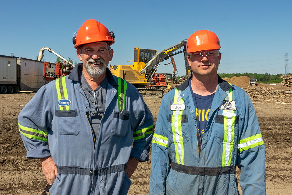 Bernard Fortin et Erik Lokseth posent devant une chargeuse Mackolines Machines & Hire 875 sur le site de la division de pâte à papier de Peace River.