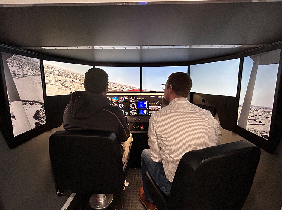 Learning to fly. Bryan Rempel, IT specialist at the De Oabeit campus in La Crete is seated next to Irfan Zardadkhan, product manager – electronic systems group (left) as he pilots the school’s flight simulator. Ironically, Irfan is an aerospace engineer.